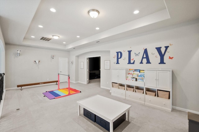 rec room featuring a tray ceiling, light colored carpet, visible vents, and arched walkways