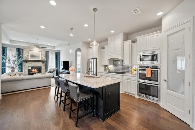 kitchen with a breakfast bar area, visible vents, arched walkways, stainless steel appliances, and a raised ceiling