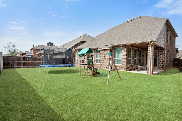 rear view of house with brick siding, a trampoline, a fenced backyard, a yard, and a patio