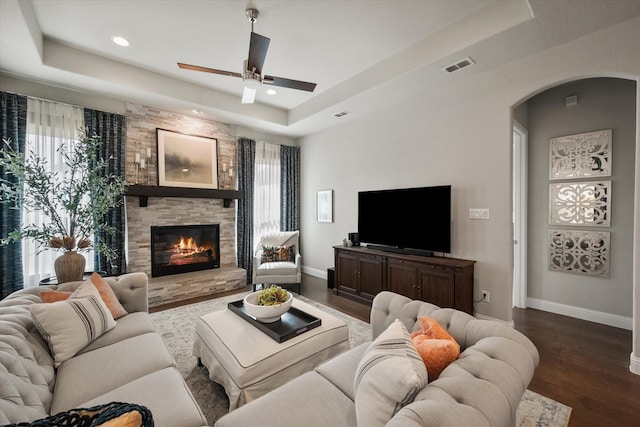 living area featuring dark wood-style floors, visible vents, a stone fireplace, and a raised ceiling