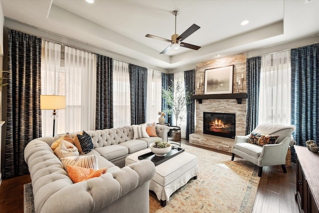 living room featuring a stone fireplace, recessed lighting, a tray ceiling, and wood finished floors