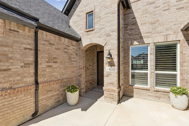 entrance to property with brick siding and roof with shingles