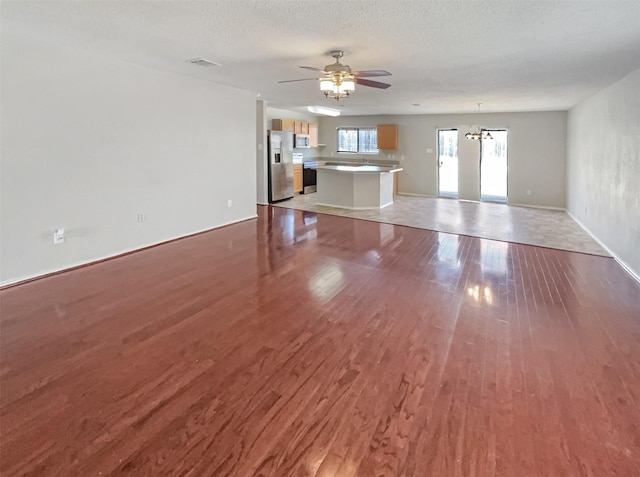 unfurnished living room featuring ceiling fan, baseboards, a textured ceiling, and wood finished floors