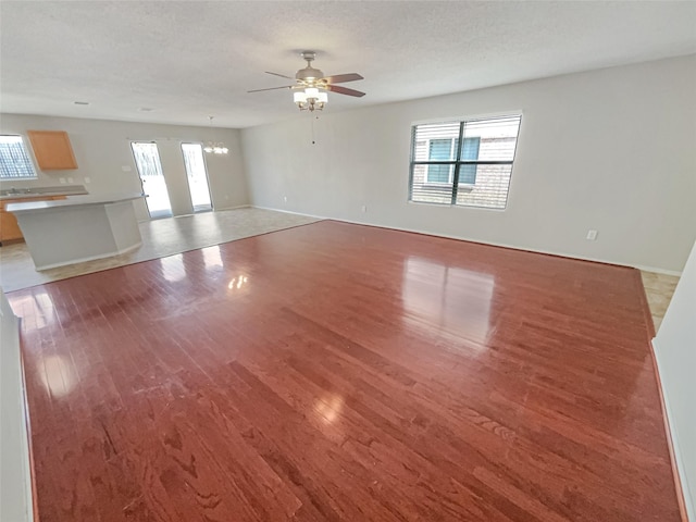 unfurnished living room featuring light wood finished floors, ceiling fan with notable chandelier, and a textured ceiling