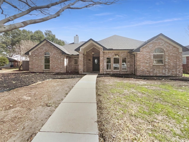 view of front of home with brick siding, a chimney, and a shingled roof