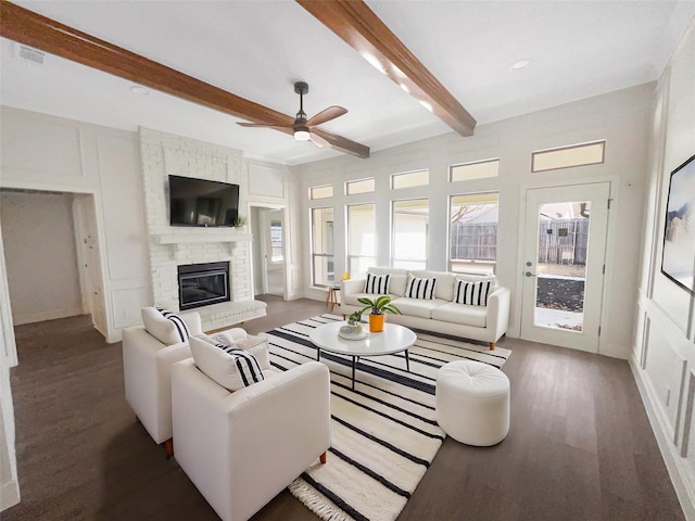 living room featuring beam ceiling, a ceiling fan, wood finished floors, a decorative wall, and a brick fireplace