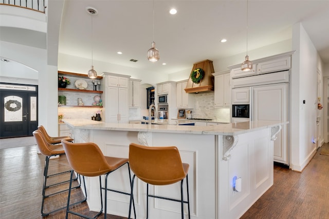 kitchen featuring visible vents, a kitchen bar, backsplash, arched walkways, and built in appliances