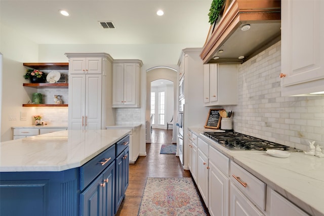 kitchen featuring visible vents, blue cabinetry, arched walkways, wall chimney range hood, and stainless steel gas cooktop