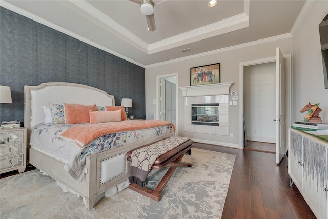 bedroom with visible vents, a tray ceiling, ornamental molding, hardwood / wood-style floors, and a fireplace