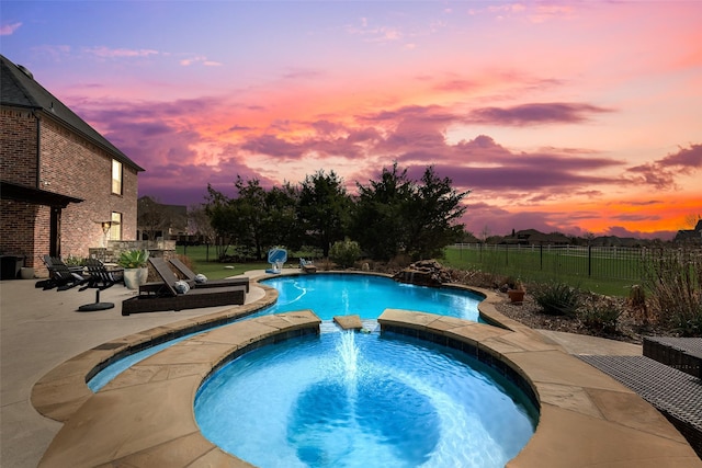 pool at dusk with a patio area, a pool with connected hot tub, and fence