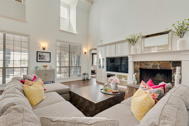 living room with arched walkways, a stone fireplace, and wood finished floors