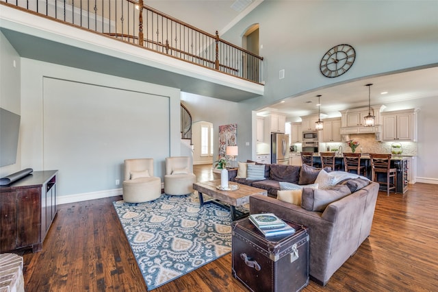 living room featuring dark wood-style floors, ornamental molding, stairs, and a towering ceiling