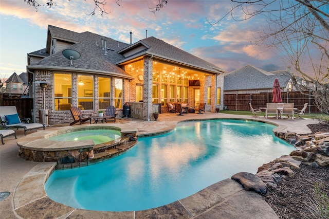 pool at dusk featuring outdoor dining space, a patio area, a pool with connected hot tub, and a fenced backyard