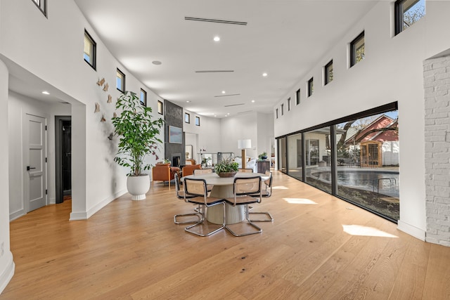 dining room with plenty of natural light, light wood-style flooring, a fireplace, and a high ceiling