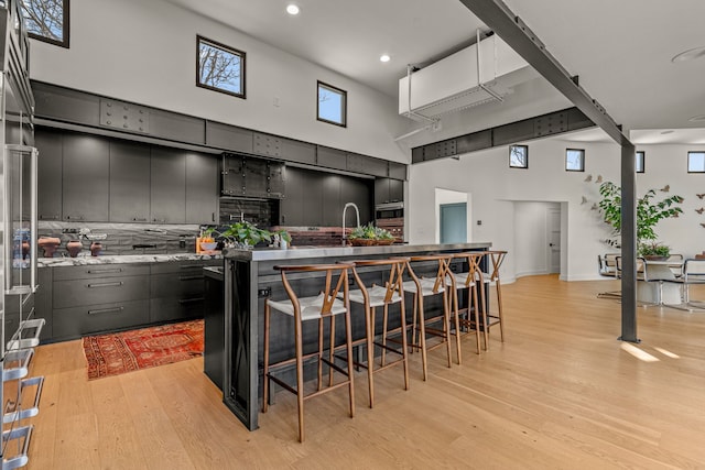 kitchen with a breakfast bar area, decorative backsplash, a large island, a towering ceiling, and light wood-type flooring