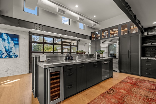 kitchen with brick wall, stainless steel countertops, wine cooler, a towering ceiling, and a sink