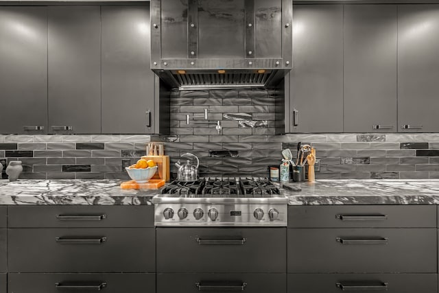 kitchen featuring gray cabinets, stone countertops, tasteful backsplash, stainless steel gas stovetop, and exhaust hood