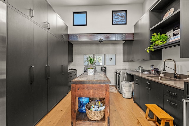 kitchen with light wood-type flooring, open shelves, a sink, dark cabinetry, and washing machine and clothes dryer