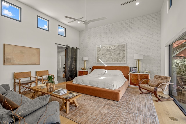 bedroom featuring a ceiling fan, wood finished floors, a barn door, a high ceiling, and brick wall