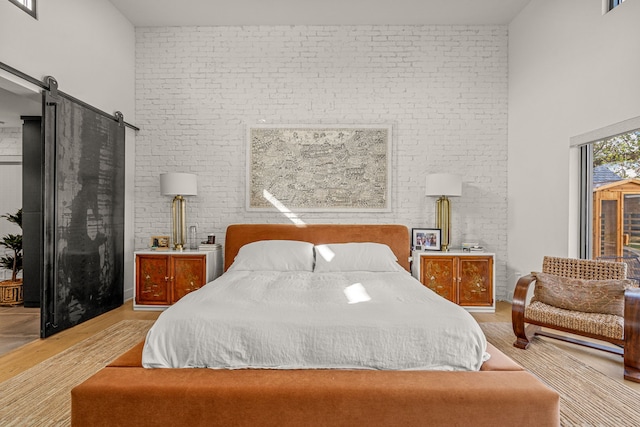 bedroom featuring a barn door, a high ceiling, wood finished floors, and brick wall