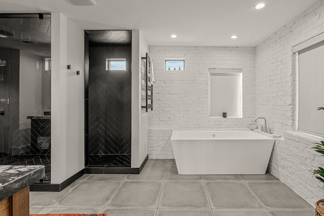 full bath featuring tile patterned flooring, a shower stall, brick wall, and a freestanding bath