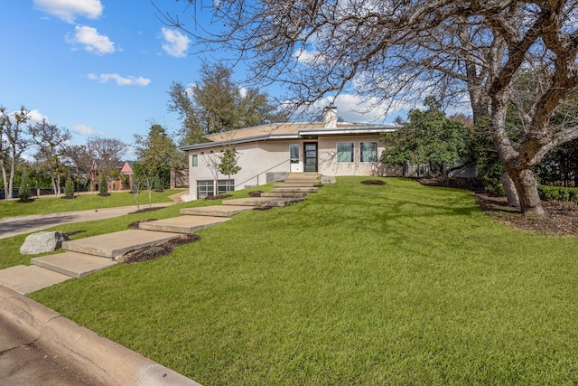 view of front of house featuring stucco siding, a chimney, and a front lawn