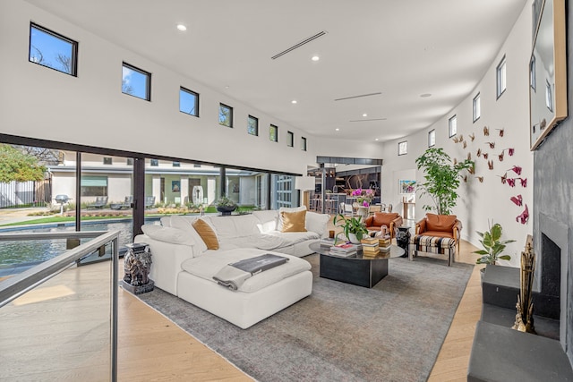 living room with visible vents, wood finished floors, recessed lighting, a high ceiling, and a fireplace