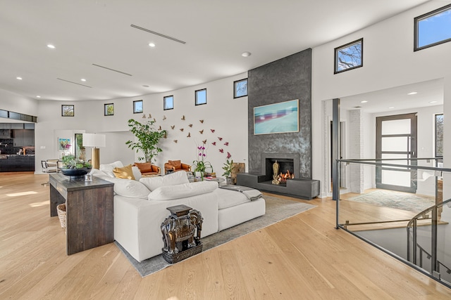 living room with a high ceiling, recessed lighting, light wood-type flooring, and a large fireplace