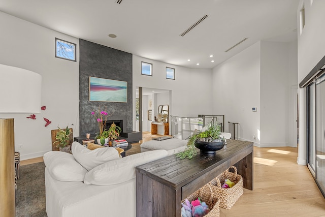 living room with visible vents, a large fireplace, light wood finished floors, baseboards, and a towering ceiling