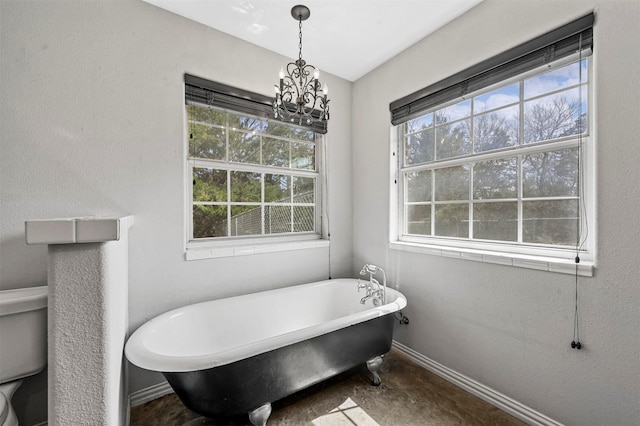 full bathroom featuring baseboards, toilet, a freestanding bath, concrete flooring, and an inviting chandelier