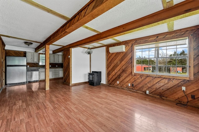 unfurnished living room with beam ceiling, a wood stove, wooden walls, and wood finished floors