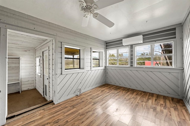 unfurnished sunroom with a wall mounted air conditioner and a ceiling fan