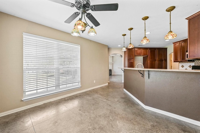 kitchen featuring backsplash, baseboards, pendant lighting, arched walkways, and a ceiling fan