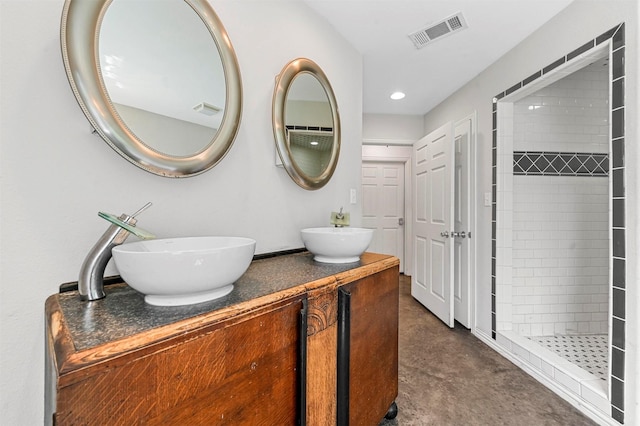 full bath with a tile shower, visible vents, concrete flooring, and a sink