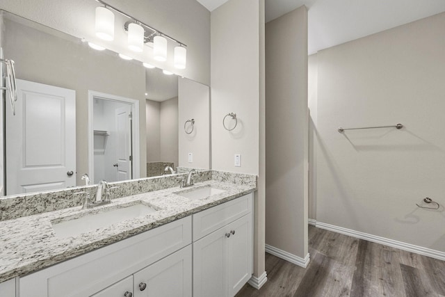 full bathroom featuring double vanity, wood finished floors, baseboards, and a sink