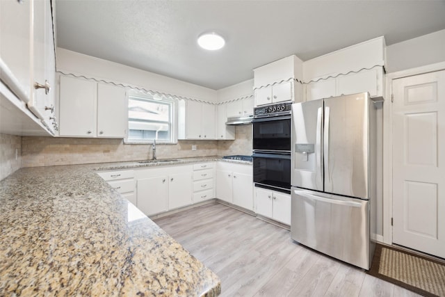 kitchen featuring backsplash, light wood-style floors, stainless steel fridge, dobule oven black, and a sink