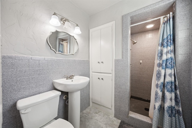 full bath featuring toilet, wainscoting, a stall shower, tile walls, and a sink