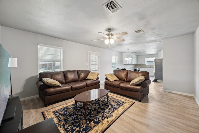 living area with a textured ceiling, baseboards, visible vents, and light wood-type flooring