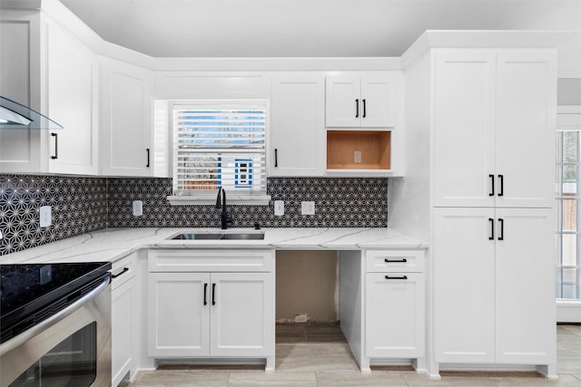 kitchen with wall chimney range hood, light stone counters, stainless steel electric range, white cabinetry, and a sink