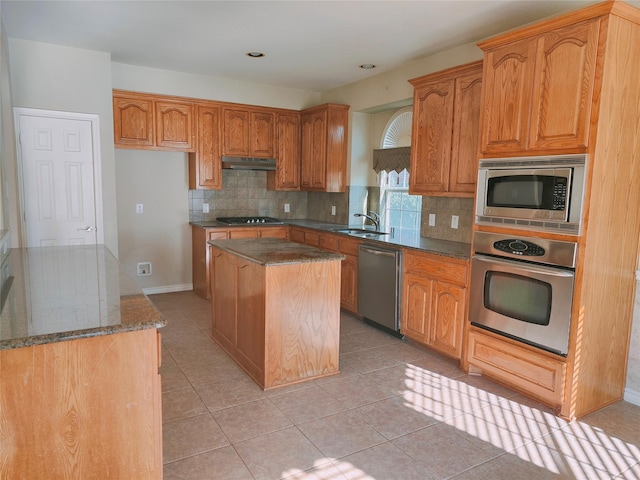 kitchen with tasteful backsplash, a kitchen island, under cabinet range hood, stainless steel appliances, and a sink