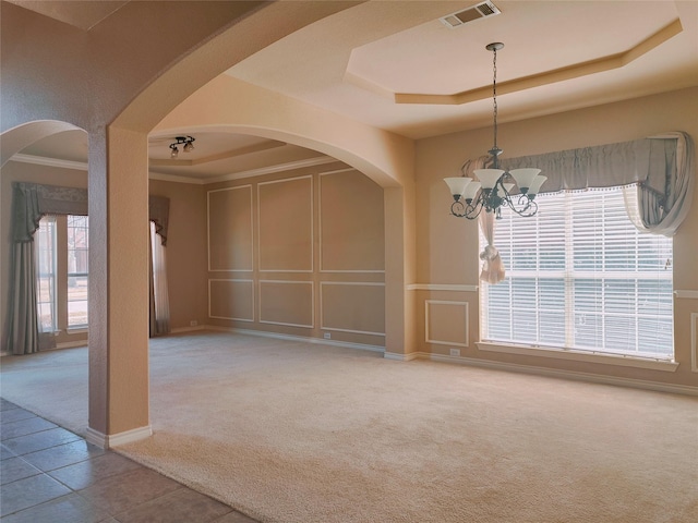 unfurnished dining area with visible vents, carpet floors, arched walkways, a raised ceiling, and a decorative wall