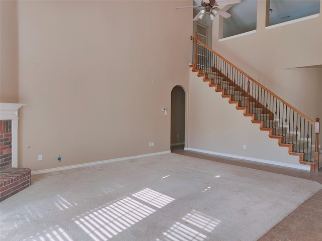 unfurnished living room featuring stairway, a ceiling fan, a high ceiling, a fireplace, and arched walkways