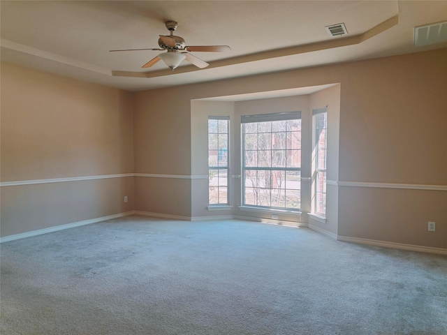 carpeted spare room with visible vents, a ceiling fan, a raised ceiling, and baseboards