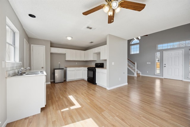 kitchen featuring black gas range oven, visible vents, light wood-style flooring, a sink, and fridge