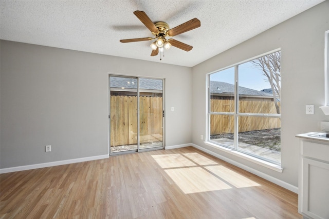 empty room with light wood finished floors, a textured ceiling, baseboards, and a ceiling fan