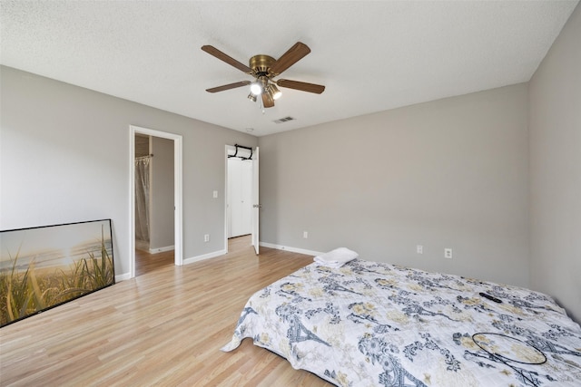 bedroom featuring wood finished floors, visible vents, baseboards, ceiling fan, and a textured ceiling