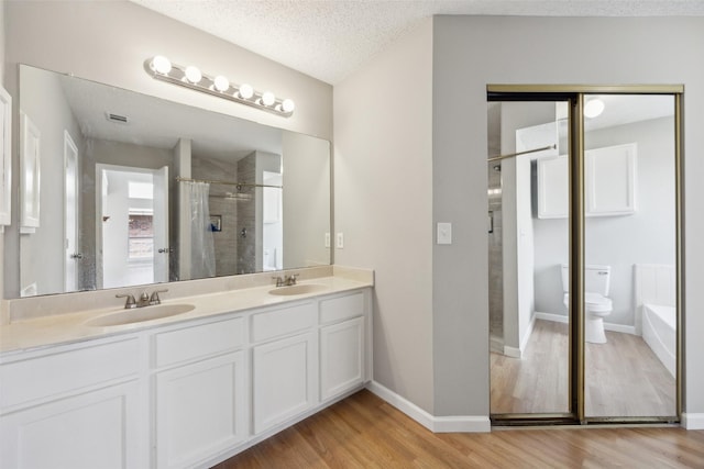 full bathroom featuring toilet, a stall shower, a sink, a textured ceiling, and wood finished floors