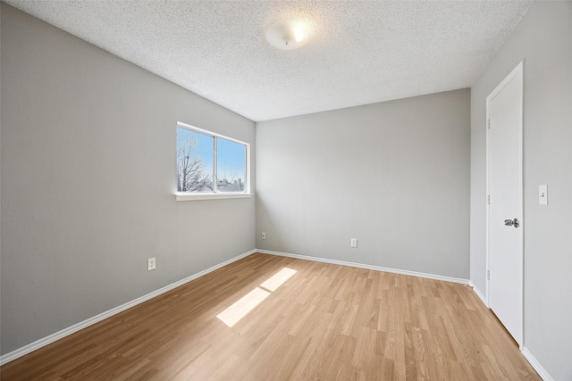 empty room with baseboards, a textured ceiling, and light wood-style floors