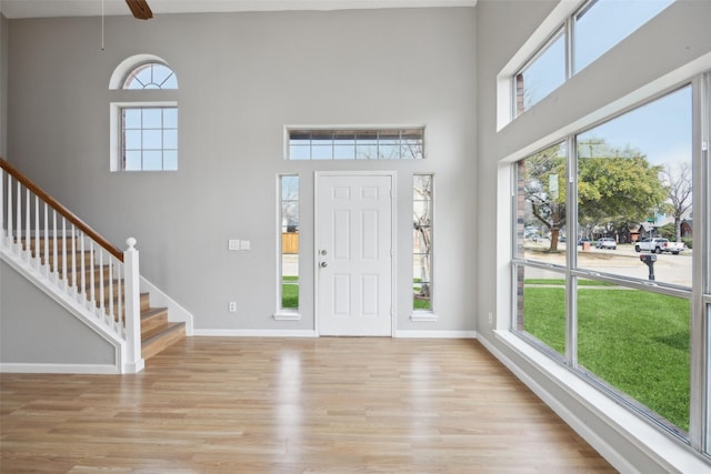 entrance foyer with stairs, a high ceiling, baseboards, and light wood finished floors