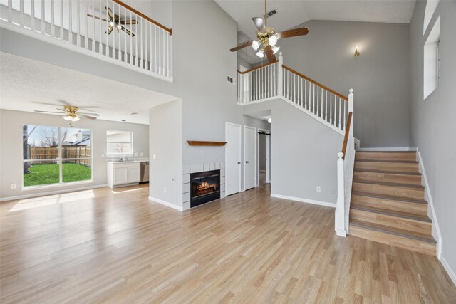 unfurnished living room with light wood-type flooring, visible vents, a fireplace, ceiling fan, and stairs